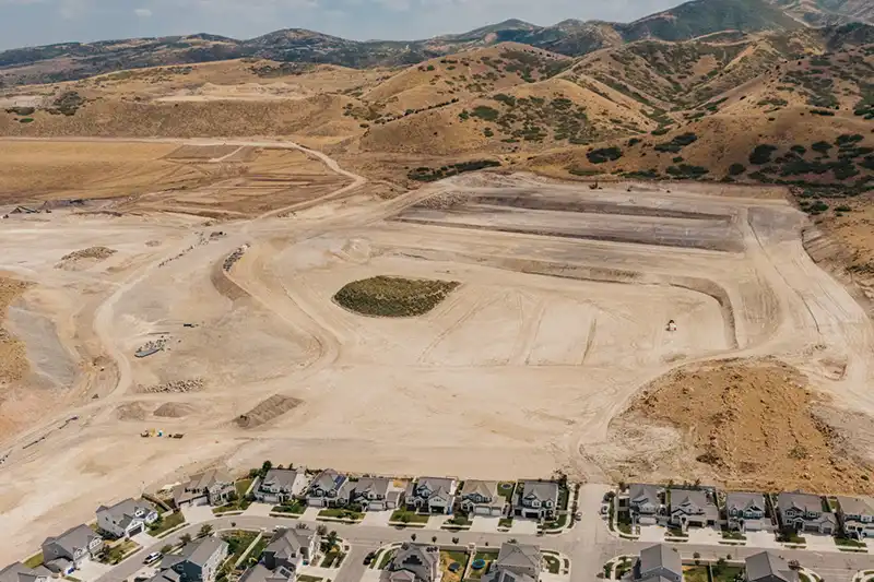 Aerial view of a graded development site with construction equipment and homes along the edge